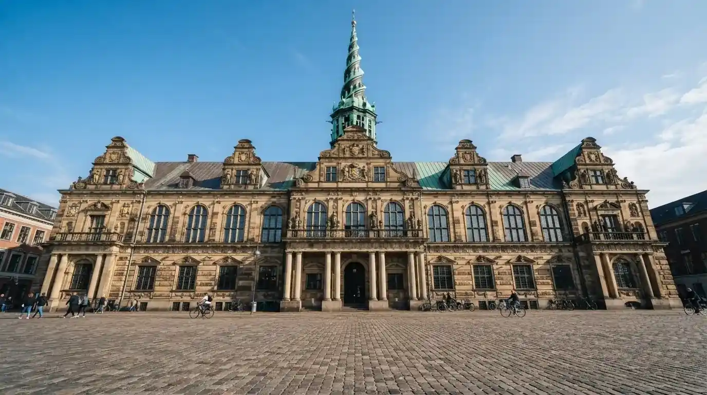 En historisk bygning i København med grøn kobbertag og kolonner i klart dagslys, set fra pladsen foran.